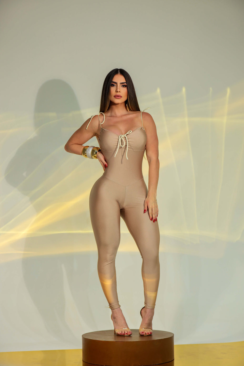 Tuta intera beige aderente da donna, modello jumpsuit con spalline sottili e dettaglio arricciato sul décolleté, indossata da modella in posa frontale