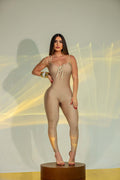 Tuta intera beige aderente da donna, modello jumpsuit con spalline sottili e dettaglio arricciato sul décolleté, indossata da modella in posa frontale