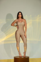 Tuta intera beige aderente da donna, modello jumpsuit con spalline sottili e dettaglio arricciato sul décolleté, indossata da modella in posa frontale